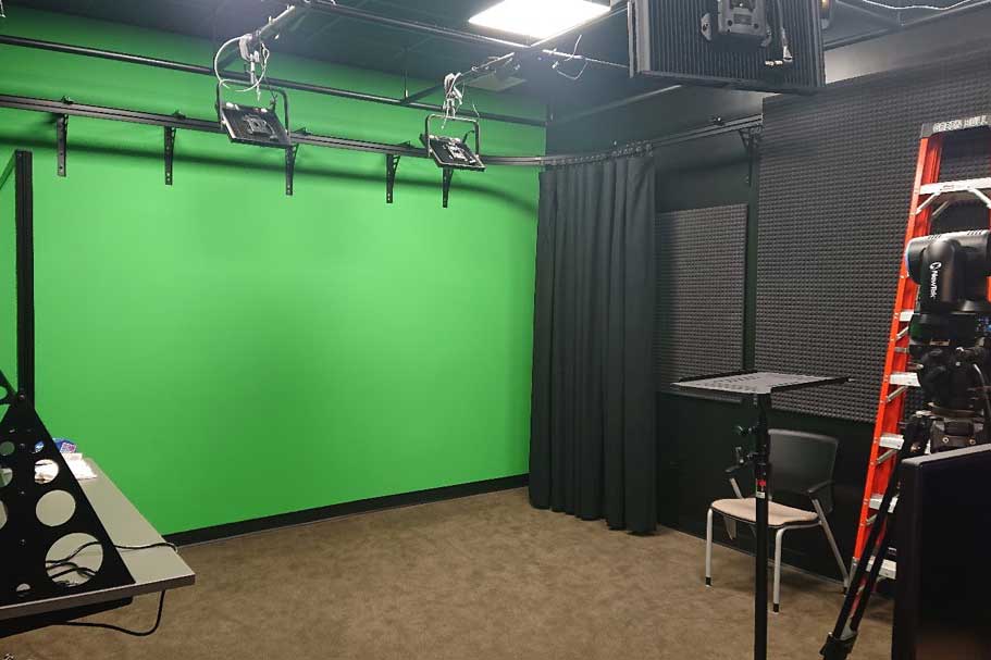 An image of a studio with a greenscreen, camera, and table.